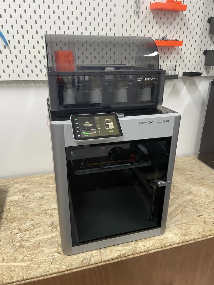 Geschlossener 3D-Drucker Bambu Lab X1 Carbon, darauf der Spulenwechsler, dahinter eine Lochwand