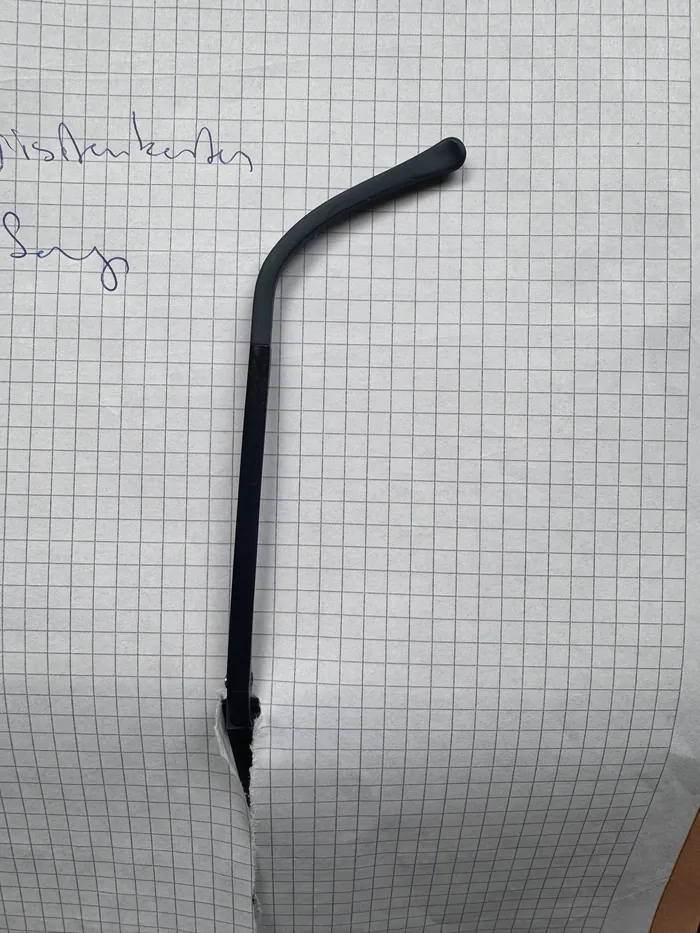Ein schwarzer Brillenbügel liegt auf Karopapier