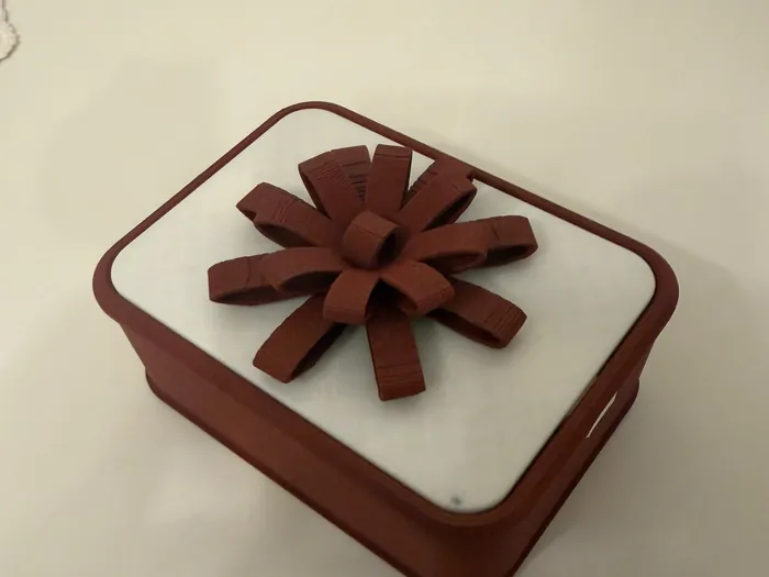 Rote Box mit weißem Deckel und einer gedruckten, dunkelroten Schleife