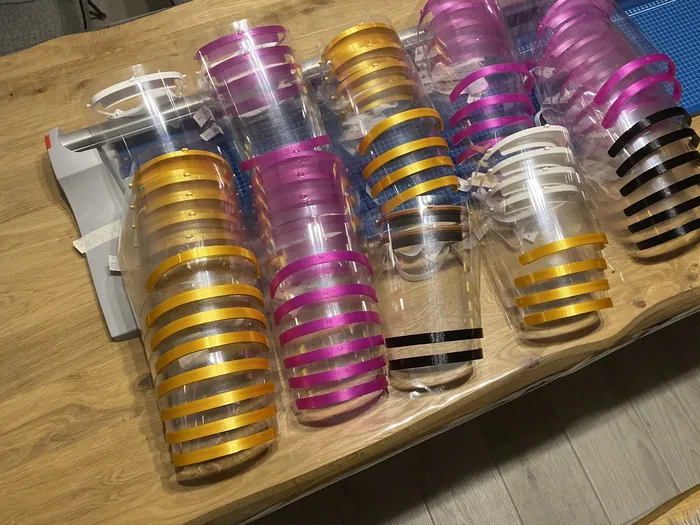 Stapel gedruckter Halterungen für Gesichtsschilde in Gelb, Pink, Weiß und Schwarz auf einem Holztisch