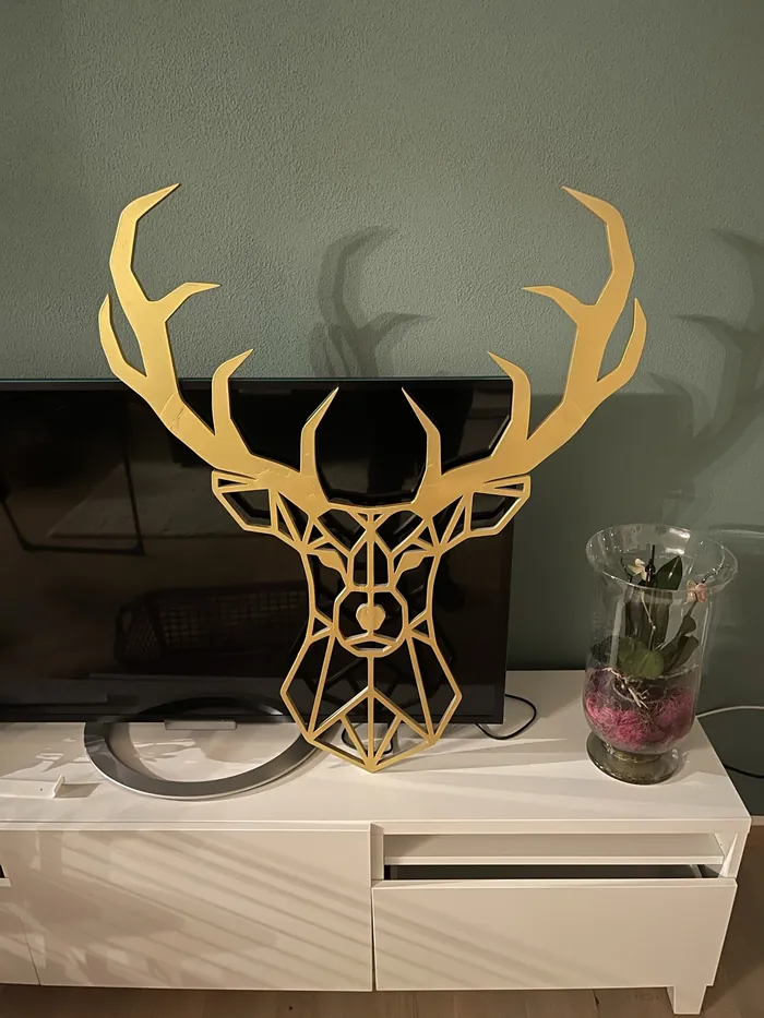 Ein goldener Hirschkopf aus Linien steht vor einer grünen Wand auf einem Sideboard