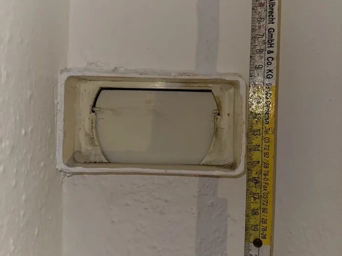 Ein Zollstock liegt an einer rechteckigen Öffnung in der Wand