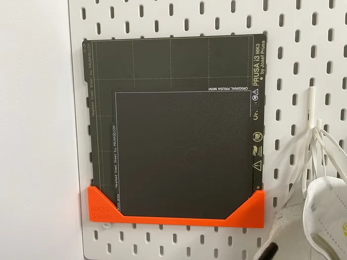 Zwei Druckplatten stehen in einem orangefarbenen Halter an einer weißen Lochwand
