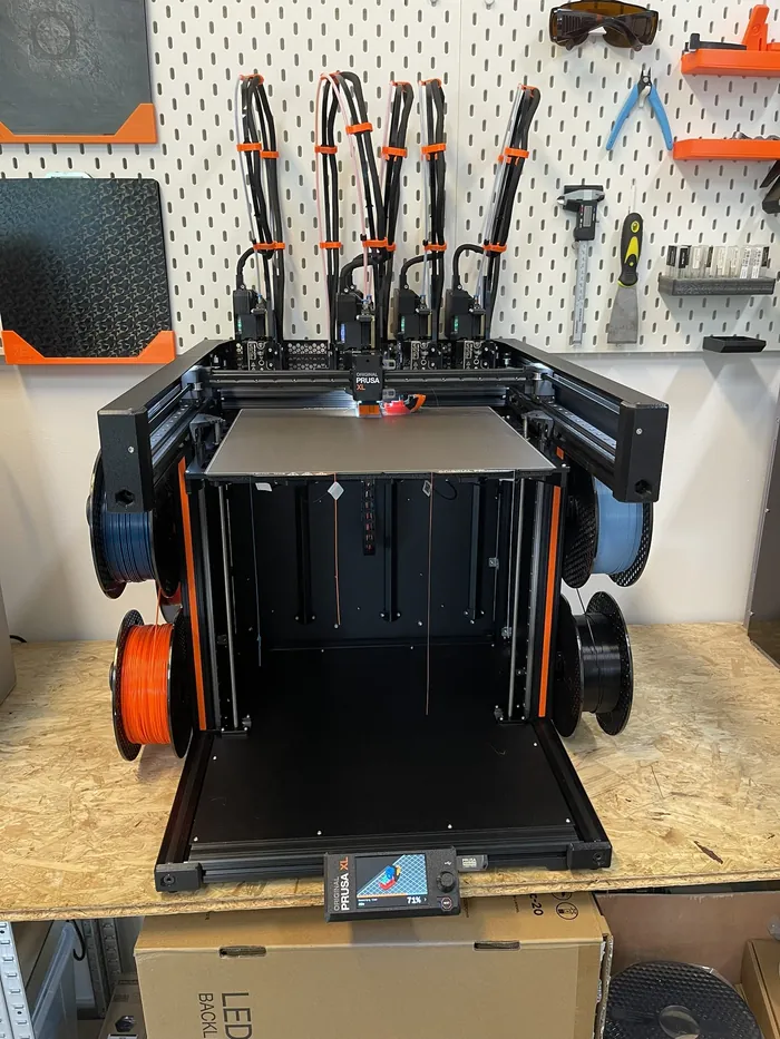 Großer 3D-Drucker mit fünf Druckköpfen vor einer Lochwand mit Werkzeug